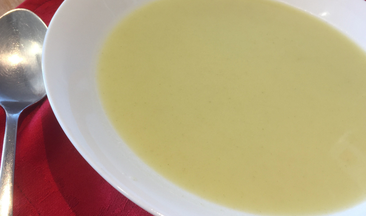 Creme de coentros com talos servido em prato branco.